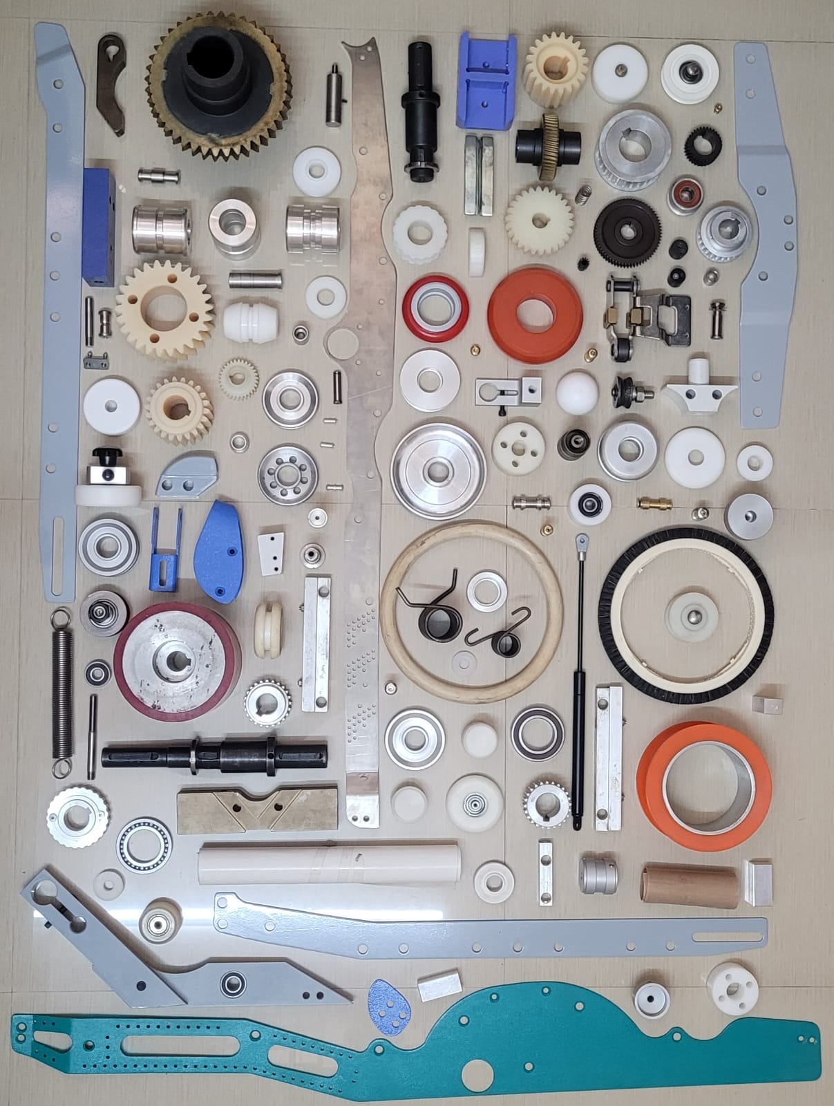 Flat-lay photograph of spare parts engineered by Sapphire Engineering Works — gears, wheels, plates and springs